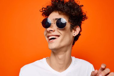 Güneş gözlüğü takan kıvırcık çocuk gençlik tarzı turuncu arka plan