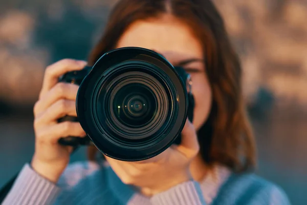 Kadın kamerayı dağlarda objektifle tutuyor ve arka planda deniz var. — Stok fotoğraf