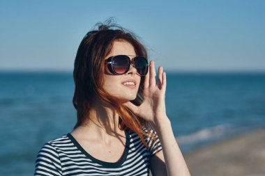 Kadın tişörtü sahilde, dağlarda deniz manzarası yakınında.