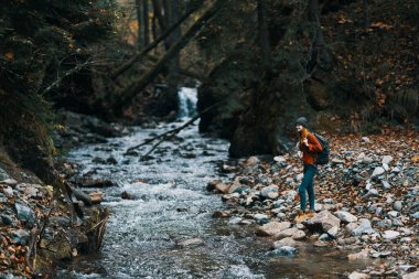 Sırt çantalı bir kadın turist nehir kıyısında yürüdü, bir dere dolusu su ve uzun ağaçlar.