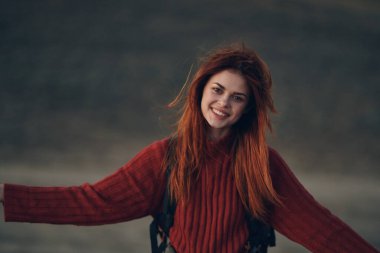 Güzel bir kadın ellerini dağlarda dolaştırarak el kol hareketi yapıyor. Kırmızı kazak seyahat ediyor.