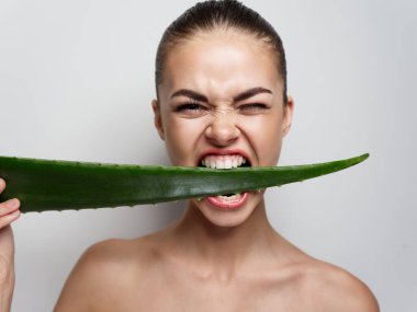 Agresif bir kadın açık arkaplanda bir aloe yaprağı kemiriyor. Temiz cilt kozmetolojisi çıplak omuzlar.