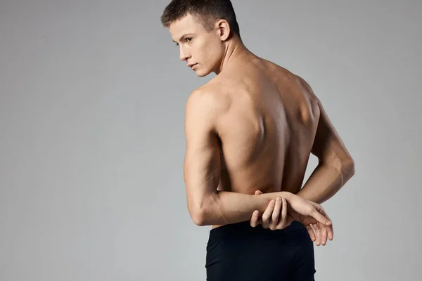 Un uomo con muscoli pompati tiene le mani dietro la schiena su uno sfondo grigio e dietro Model Copy Space — Foto Stock