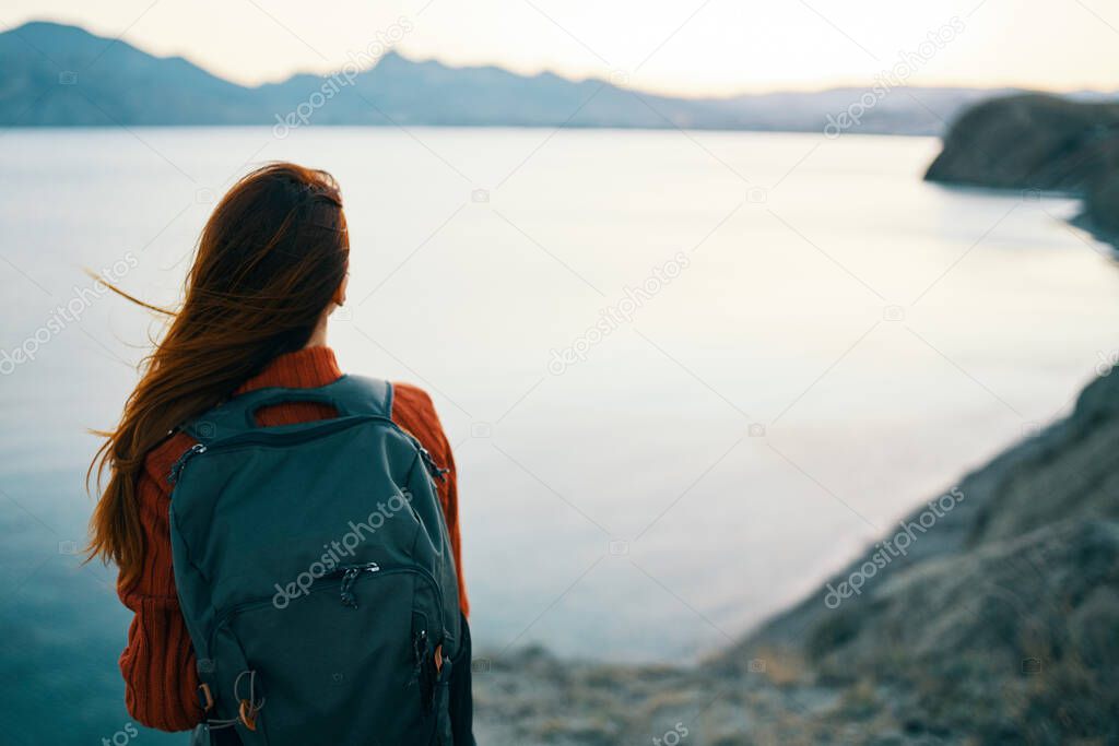 woman in red sweater with backpack and travel tourism sea mountains back view