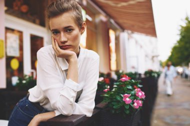 Binanın yanında kısa saçlı bir kadın ve çiçek desenli bir cadde.