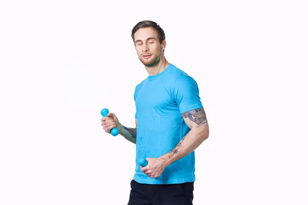Um homem fazendo exercícios com halteres em um fundo claro em uma camiseta azul e calças — Fotografia de Stock