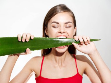 Kadın kırmızı tişörtlü bir arka planda aloe yaprağıyla yaşıyor. Vitaminler temiz cilt kozmetolojisi.