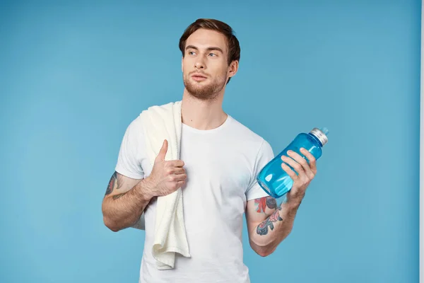 Uomo sportivo con asciugamano sulla spalla bottiglia d'acqua allenamento fitness sfondo blu — Foto Stock