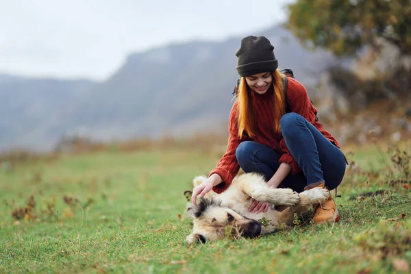 Mulher caminhante com uma mochila na natureza nas montanhas é jogado com uma amizade cão — Fotografia de Stock