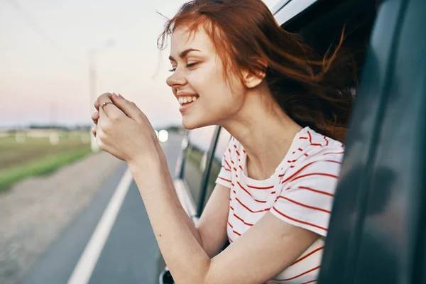 Χαρούμενη γυναίκα με κόκκινα μαλλιά κοιτάζει έξω από το παράθυρο του αυτοκινήτου στο δρόμο στις καλοκαιρινές διακοπές χαλαρώστε — Φωτογραφία Αρχείου