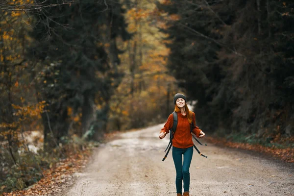 Donna con zaino sulla strada nella foresta in autunno paesaggio alto alberi modello — Foto Stock