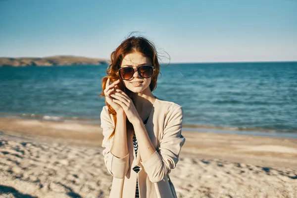 ジャケットを着た感情的な赤い髪の女性は海の近くに自然に顔の近くに手を保持します — ストック写真