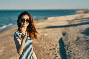 Kumsalda, deniz kenarında güneş gözlüklü, kızıl saçlı bir kadın.