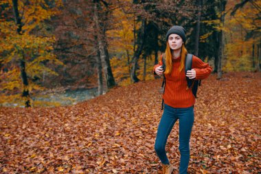 Sonbahar ormanında sırt çantalı bir gezgin ve kazak kotu düşmüş göl ağaçları.