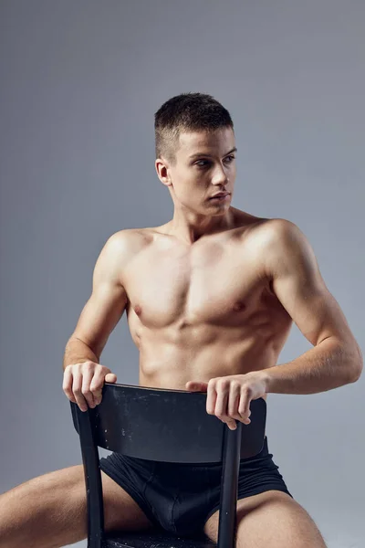 Athletic man in black panties pumped up body sits on a chair — Stock Photo, Image