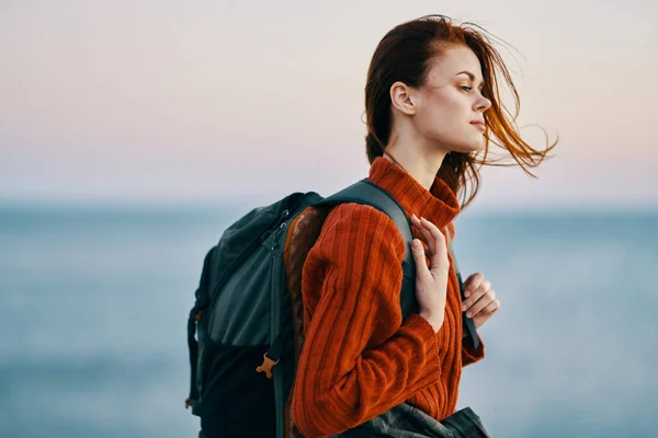 Donna escursionista donna con uno zaino vicino al mare in montagna in natura e un modello di maglione rosso — Foto Stock