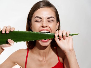 Güzel bir kadın kırmızı tişörtlü aloe yaprağını ısırıyor.