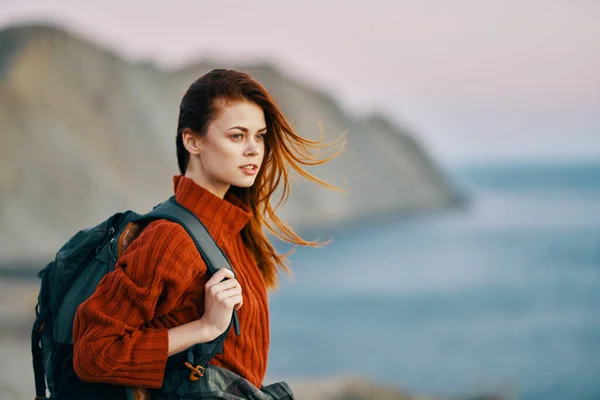 Reisende in einem roten Pullover am Meer in der Natur mit einem Rucksack auf dem Rücken und Bergen im Hintergrund — Stockfoto