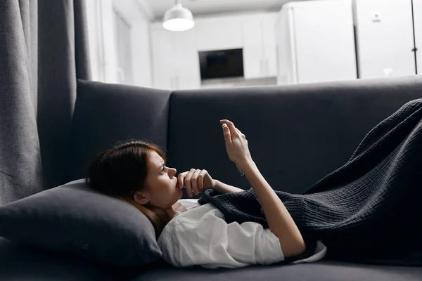 Mujer descansando acostada en el sofá con un teléfono móvil en la mano —  Fotos de Stock