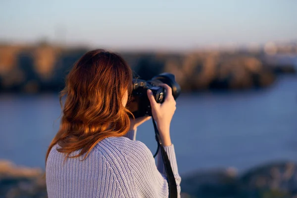 Woman in the mountains near the sea at sunset with a professional camera in her hands — Stock Photo, Image