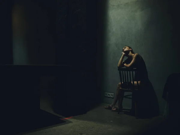 Kobieta siedzi na krześle w ciemnym pokoju samotność spada lekka sylwetka — Zdjęcie stockowe