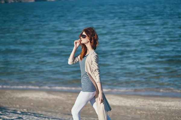 Mujer en gafas de sol y pantalones caminando por la playa cerca del mar en las montañas —  Fotos de Stock