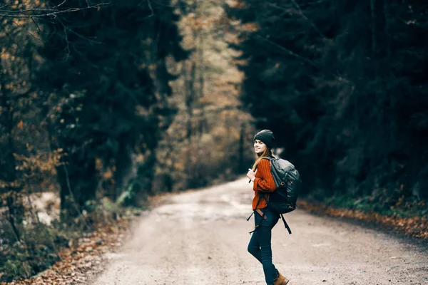 Donna con zaino sulla strada nella foresta in autunno paesaggio alto alberi modello — Foto Stock