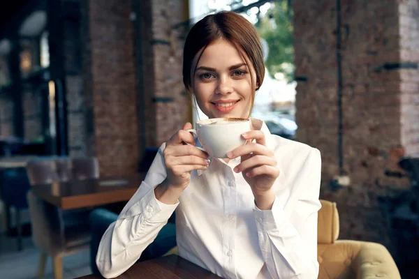 Mulher de negócios bonita na camisa branca senta-se em um café com uma xícara de café — Fotografia de Stock