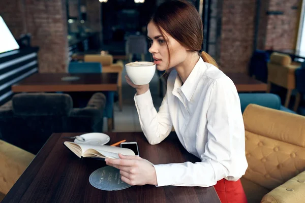 Mulher em saia camisa à mesa no café xícara na mão e caneta notepad — Fotografia de Stock