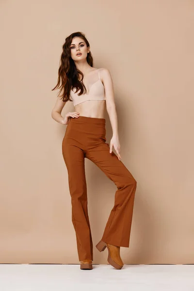 Bonita mujer en pantalones y sujetador en fondo beige botas de pelo rojo modelo —  Fotos de Stock