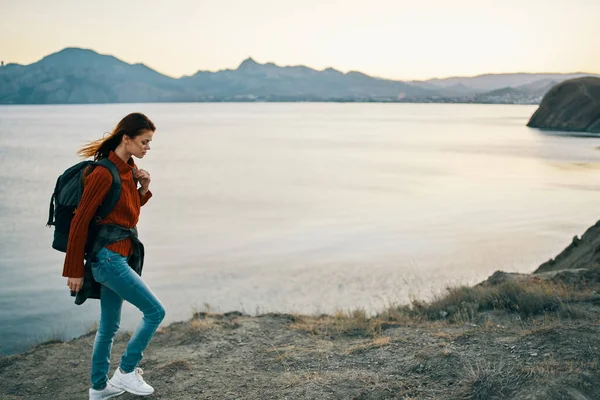 Viaggiatore in maglione con zaino in jeans e scarpe da ginnastica sulla spiaggia vicino al mare in montagna — Foto Stock