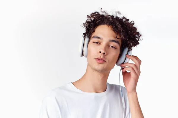 Hombre emocional con el pelo rizado y en los auriculares escucha música fondo de luz — Foto de Stock