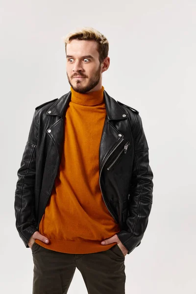 Een blonde man in een oranje trui en een modieuze jas houdt zijn handen in zijn zakken en kijkt naar de zijkanten — Stockfoto