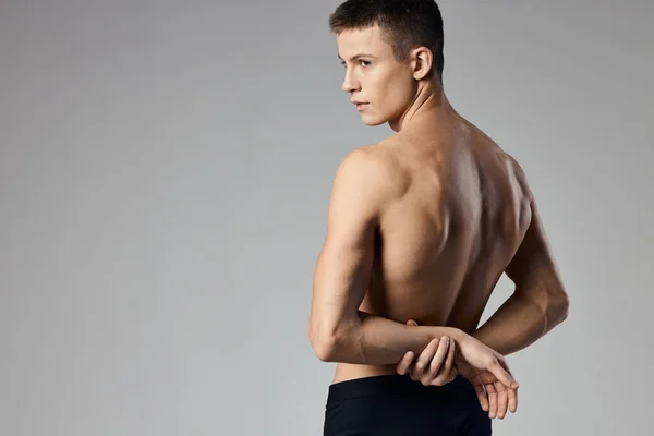 Человек с накачанными мышцами держит руки за спиной на сером фоне и за моделью — стоковое фото