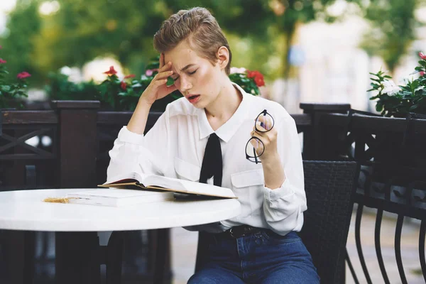 Kvinna läser en bok vid ett bord i en restaurang utbildning känslor glasögon blommor i bakgrunden — Stockfoto