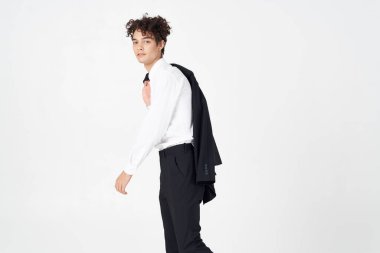 Klasik takım elbiseli, elinde ceketi olan, açık renk bir arka planı olan, kıvırcık saçlı, şık saçlı bir adam.