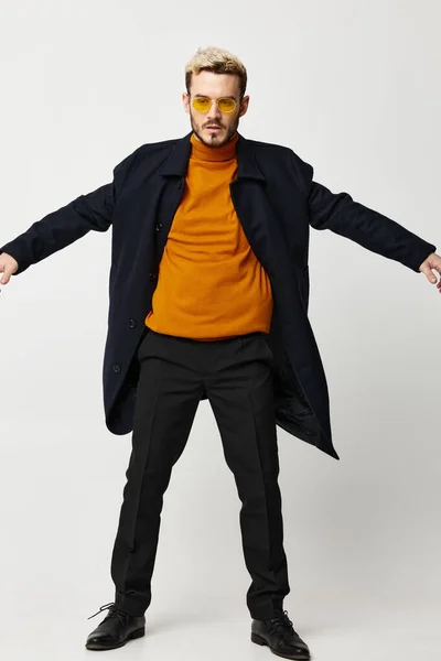 a blond man in a black coat and pants orange sweater trend of the season