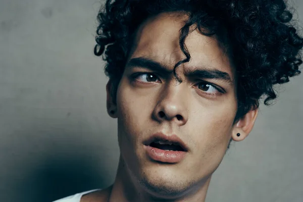 Ritratto di un bel ragazzo con i capelli ricci su uno sfondo grigio bianco t-shirt modello close-up — Foto Stock