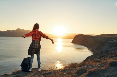 Elleri havada, gün batımında geriye bakan kadın turist.