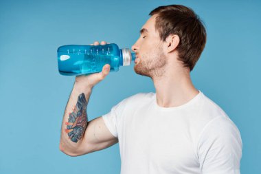 Kollarında dövmeleri olan sportif bir adam. Mavi çalışma suyu şişesi.