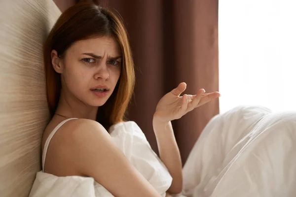 Mujer indignada haciendo gestos con las manos en la cama bajo las sábanas cerca de la ventana —  Fotos de Stock