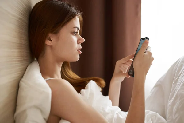 一个女人躺在床上 看着旁边的手机屏幕 高质量的照片 — 图库照片
