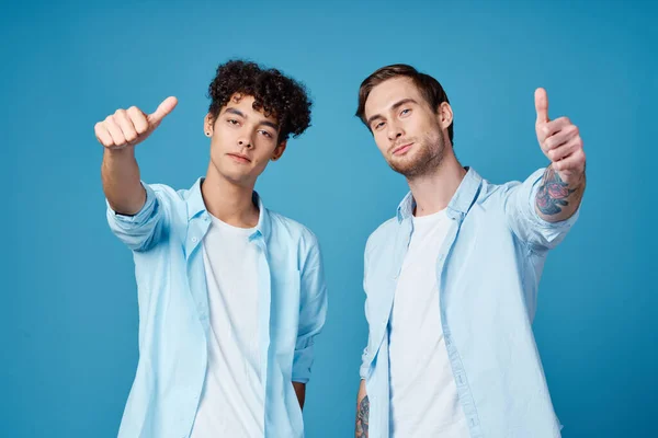 Молодые парни в одних рубашках и футболках жестикулируют руками на синем фоне друзей — стоковое фото