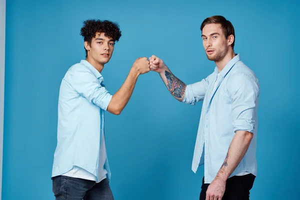 Un hombre con un tatuaje se da la mano con un chico rizado en un fondo azul amigos comunicación — Foto de Stock