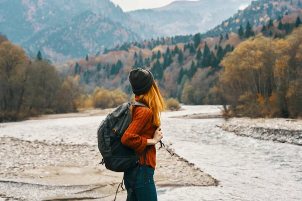 Mulher em suéter com uma mochila descansar nas montanhas perto do rio no outono na natureza e modelo de árvores altas — Fotografia de Stock