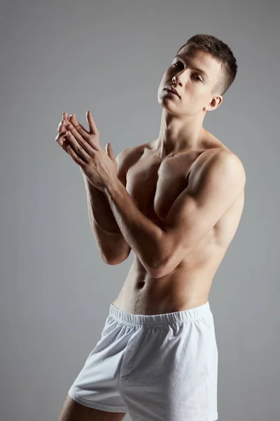 Чоловік культурист в білих шортах жестикулює руками на сірому фоні спортивної фітнес — стокове фото