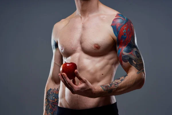 Hombre con un tatuaje sostiene una manzana en sus manos torso desnudo bombeado músculos bíceps prensa — Foto de Stock