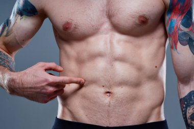 Karnında küpleri olan sporcu vücut kaslarını şişirmiş dövmeler çıplak gözle görünür.