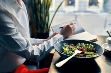 Tabak çatallı bir not defterinde leziz bir yemek salatası ve gömlek kafe içinde bir kadın.
