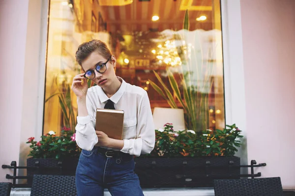 Vzdělaná žena s knihou a brýlemi sedí na křesle v kavárně exteriér — Stock fotografie